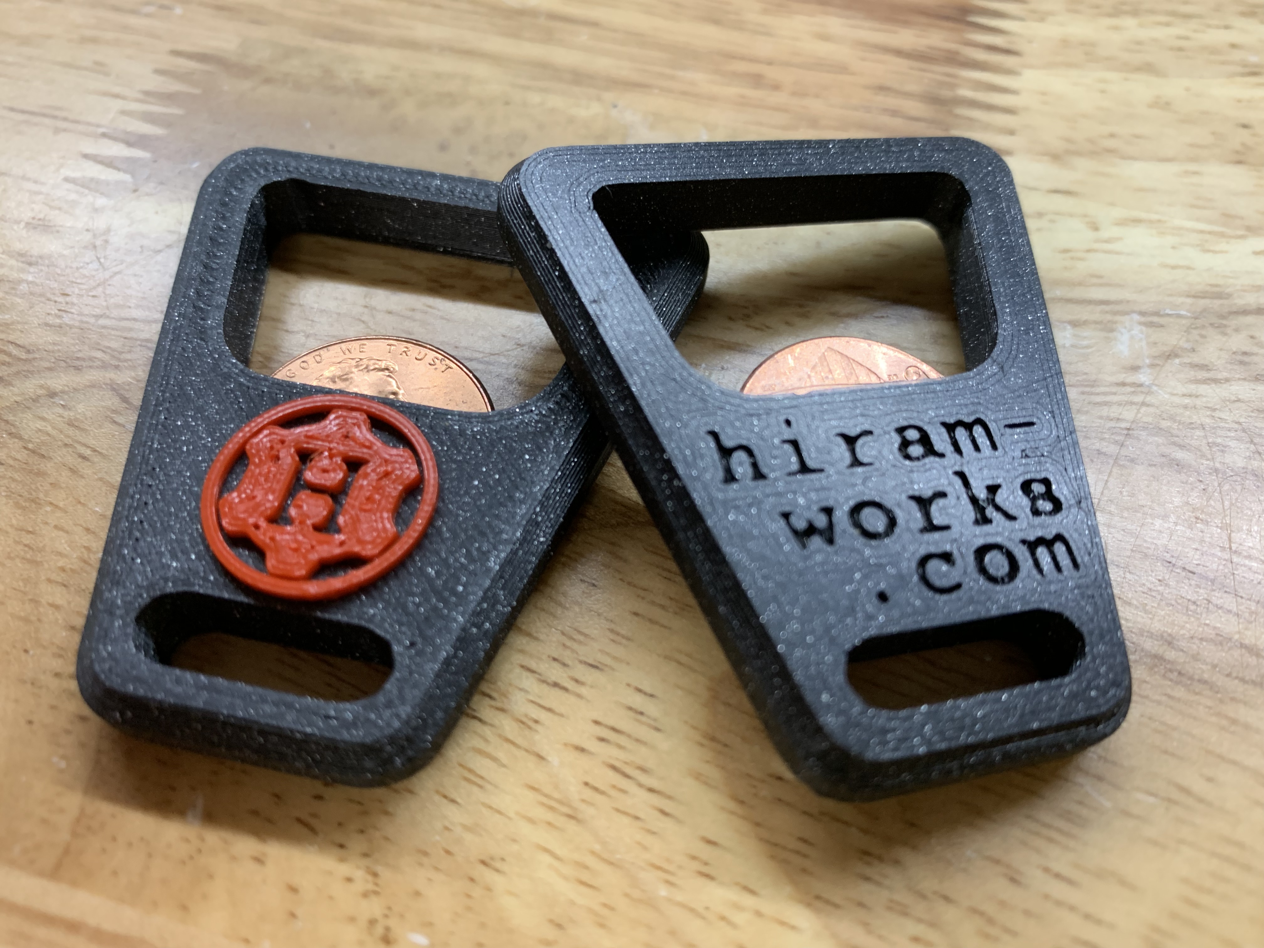 Two 3D-printed Hiram-Works branded bottle openers &mdash; one with the compass-mark logo, one with the wordmark.